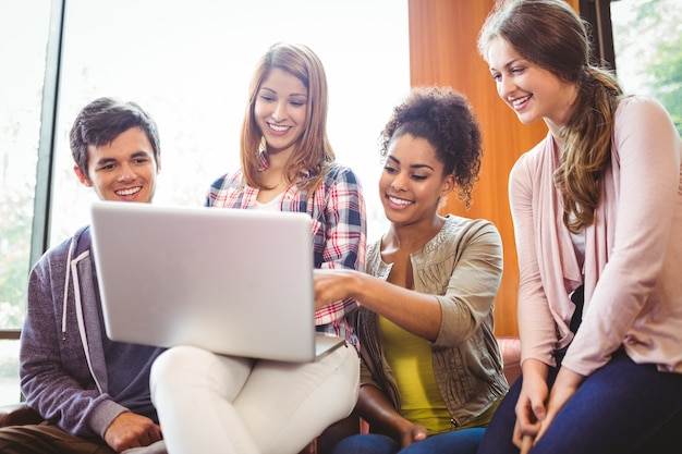 Lächelnde Studenten, die auf Couch unter Verwendung des Laptops sitzen