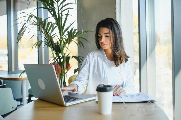 Lächelnde Studentin lernt online mit Skype Lehrerin glückliche junge Frau lernt Sprache hören Vorlesung ansehen Webinar schreiben Notizen schauen auf Laptop sitzen im Café Fernbildung