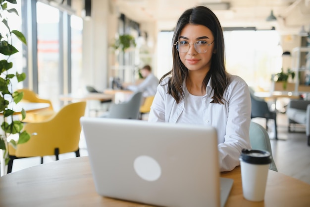 Lächelnde Studentin lernt online mit Skype Lehrerin glückliche junge Frau lernt Sprache hören Vorlesung ansehen Webinar schreiben Notizen schauen auf Laptop sitzen im Café Fernbildung