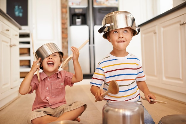 Lächelnde Töpfe und Spielen mit Kindern in der Küche sorgen für Fantasie, Fantasie und Spiele. Geschwister knüpfen und glücklich mit Kindern sein, und Küchenutensilien auf dem Boden des Einfamilienhauses sorgen für Musik, Lärm und Glück