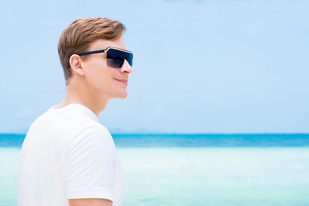 Lächelnde tragende Sonnenbrille des zufälligen touristischen Mannes am Strand in den Sommerferien