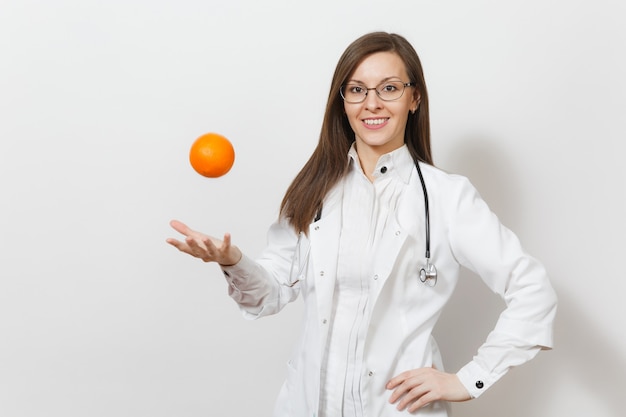 Lächelnde überzeugte schöne junge Doktorfrau mit Stethoskop, Gläser lokalisiert auf weißem Hintergrund. Ärztin im medizinischen Kittel, die Orange aufwirft. Gesundheitspersonal, Gesundheit, Medizinkonzept.