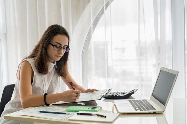 Lächelnde und junge Frau, die im Büro mit Dokumenten arbeitet