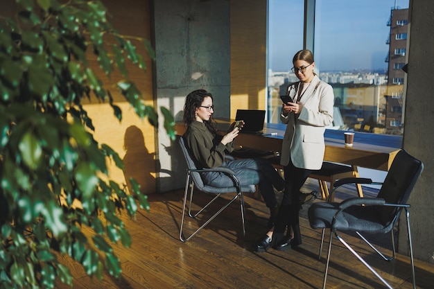 Lächelnde weibliche Kollegen, die drinnen am Tisch zusammenarbeiten Frau, die eine Brille trägt und Laptop verwendet und Partner zeigt Geschäftsbeziehungen von Serel-Kollegen im Büro Teamarbeit von Kollegen