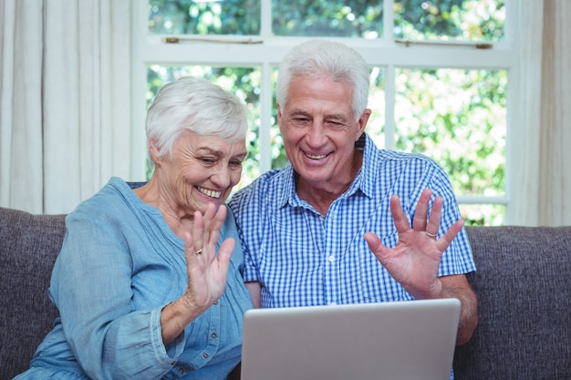 Lächelnde wellenartig bewegende Hand der älteren Paare bei der Anwendung des Laptops