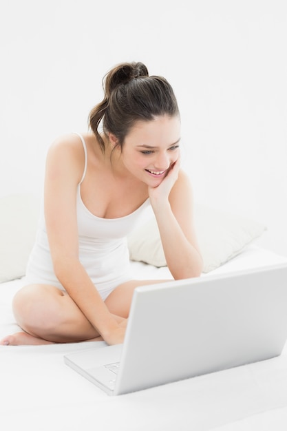 Lächelnde zufällige Frau mit Laptop auf Bett