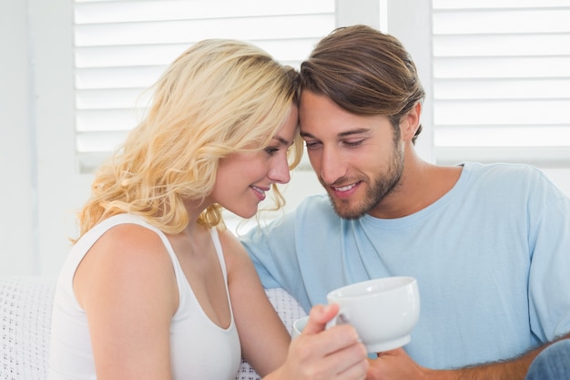 Lächelnde zufällige Paare, die auf der Couch trinkt Kaffee sitzen