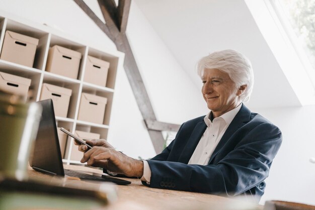 Lächelnder älterer Geschäftsmann benutzt Laptop in seinem Büro