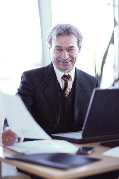 Lächelnder älterer Geschäftsmann, der an seinem Schreibtisch sitzt