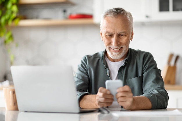 Lächelnder älterer Mann, der zu Hause Smartphone und Laptop-Computer benutzt
