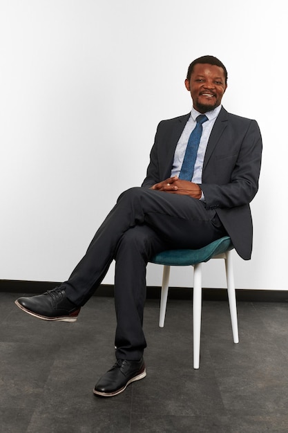 Lächelnder afrikanisch-amerikanischer schwarzer Mann im Business-Anzug, der mit gekreuzten Fingern auf einem Stuhl sitzt