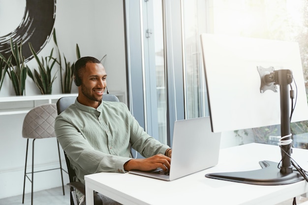 Lächelnder afrikanischer Geschäftsmann, der am Laptop arbeitet, während er in einem modernen Büro sitzt