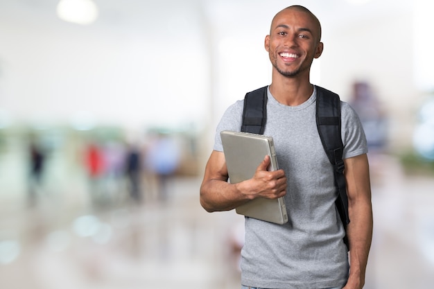 Lächelnder afrikanischer Studentenmann mit Laptop, Mallhintergrund, bokeh