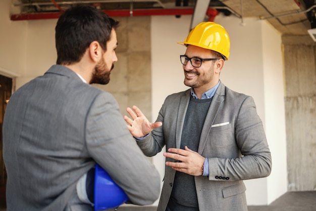 Lächelnder Architekt, der mit Investor spricht, während er im Bauprozess im Gebäude steht.