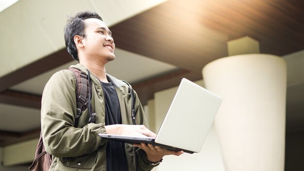 Lächelnder asiatischer Mann, der einen Rucksack mit einem Laptop trägt