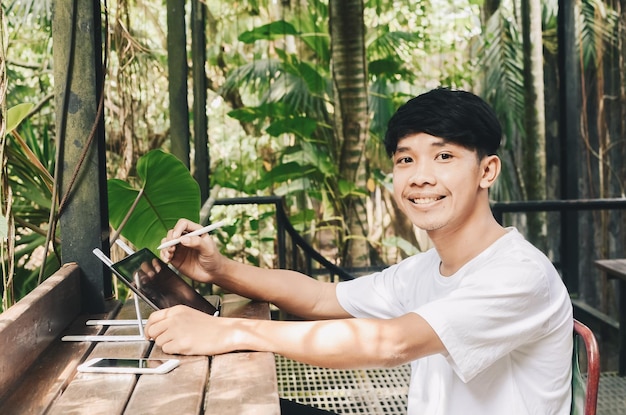 Lächelnder asiatischer Mann, der mit einem Tablet in einem Café an einer Aufgabe arbeitet