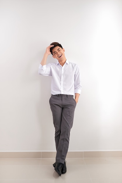 Lächelnder asiatischer Mann in Hosen und Hemd, der nahe leerer Wand steht. Konzept des Geschäftsmannes. Attrappe, Lehrmodell, Simulation