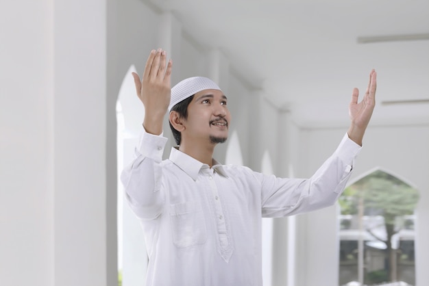 Lächelnder asiatischer moslemischer Mann mit Trachtenkleid beten zum Gott