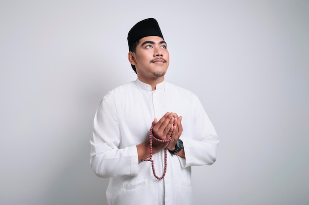 Lächelnder asiatischer muslimischer Mann in weißer Gebetskleidung, der zu Gott betet
