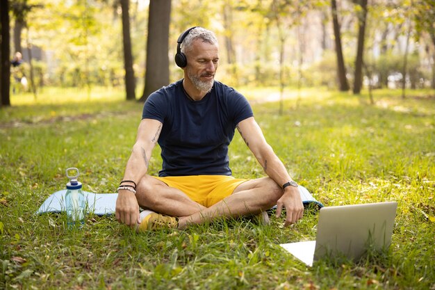 Lächelnder athletischer Mann, der online Yoga in der Natur praktiziert