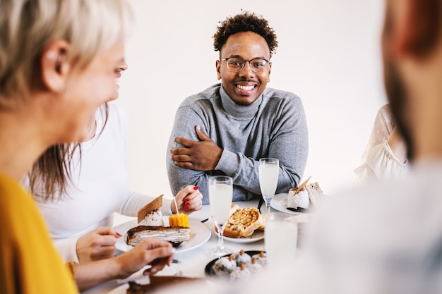 Lächelnder attraktiver Afroamerikanermann, der am Esstisch mit Freunden zum Mittagessen sitzt und lächelt