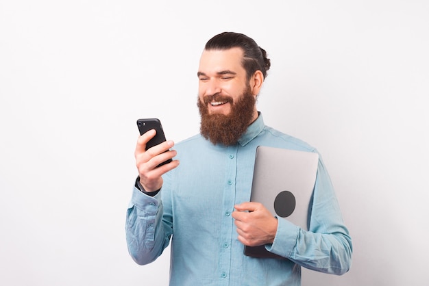 Lächelnder bärtiger Mann benutzt sein Telefon, während er Laptop hält.