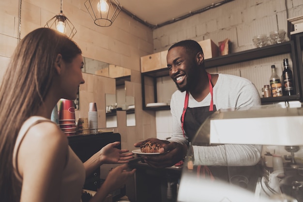 Lächelnder barista Mann gibt einem Mädchen ihre Bestellung