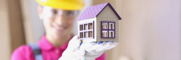 Lächelnder Baumeister im Schutzhelm hält Miniaturhaus