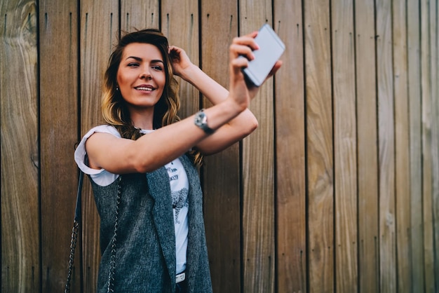 lächelnder blogger, der für die kamera posiert, die selfie auf einem modernen telefon macht, um das profilbild zu aktualisieren