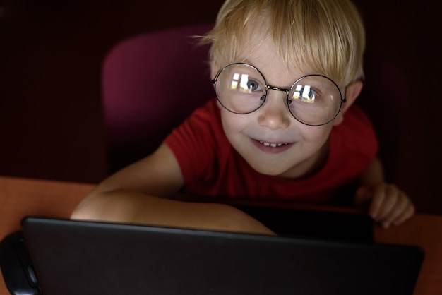 Lächelnder blonder Junge mit Brille an einem Laptop