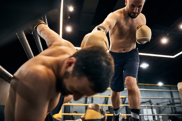 Lächelnder Boxer, der seinem verletzten Sparringspartner in der Ecke eines Rings einen letzten Schlag versetzt