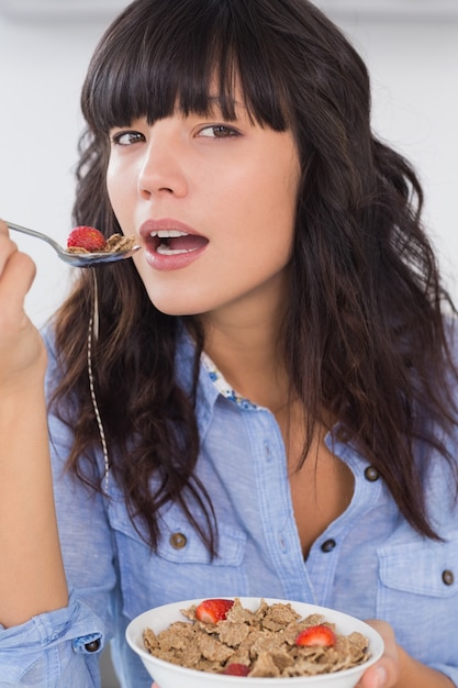 Foto lächelnder brunette, der schüssel getreide und frucht isst