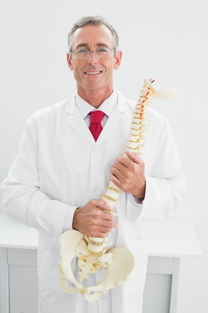 Lächelnder Doktor, der skeleton Modell im Büro hält