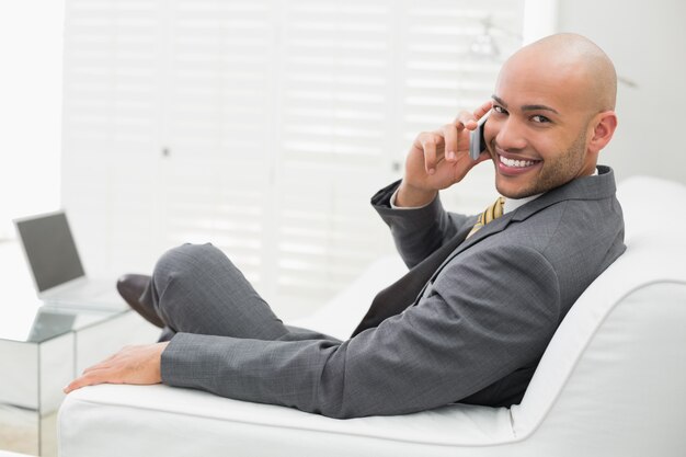 Lächelnder eleganter Geschäftsmann, der zu Hause Mobiltelefon auf Sofa verwendet