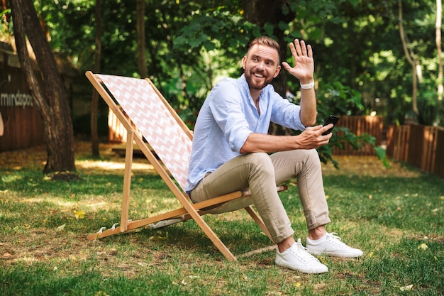 Lächelnder emotionaler junger bärtiger Mann, der Handy verwendet