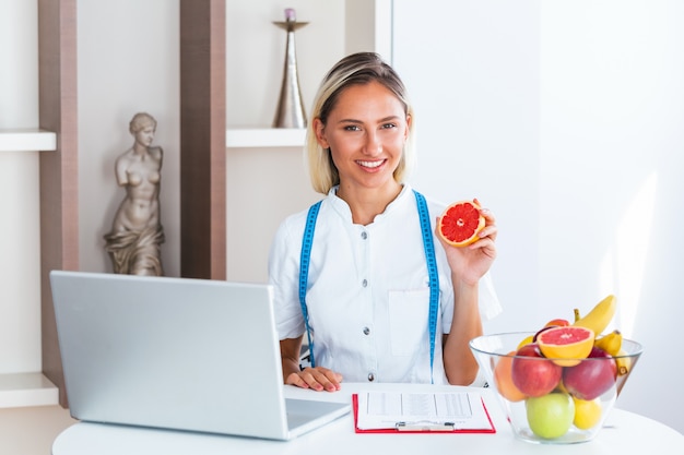 Lächelnder Ernährungswissenschaftler im Büro, das eine Frucht hält