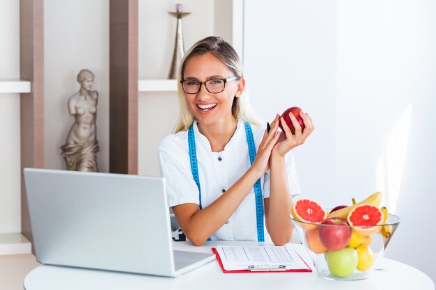 Lächelnder Ernährungswissenschaftler im Büro, das eine Frucht hält