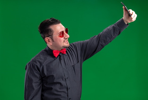 Lächelnder erwachsener slawischer Mann in roter Sonnenbrille, der ein Selfie am Telefon macht