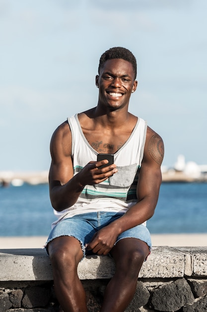 Lächelnder ethnischer Mann mit Smartphone am Damm