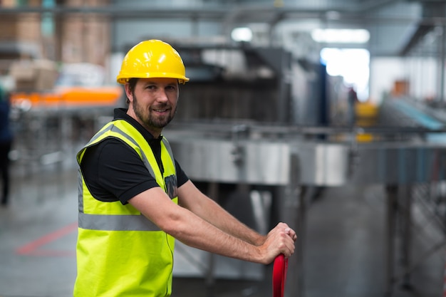 Lächelnder Fabrikarbeiter, der Wagen in Fabrik zieht