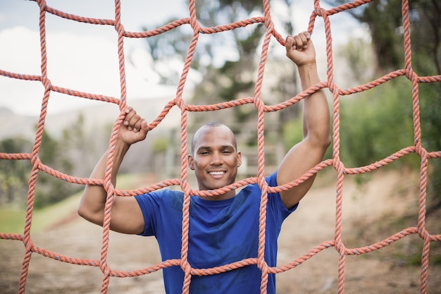 Lächelnder fit Mann, der ein Netz während des Hindernislaufs im Bootcamp klettert