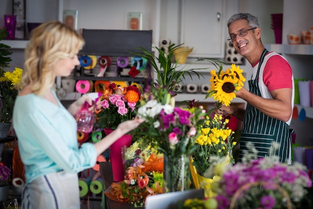 Lächelnder Florist, der Wasser auf Blumen im Blumenladen sprüht