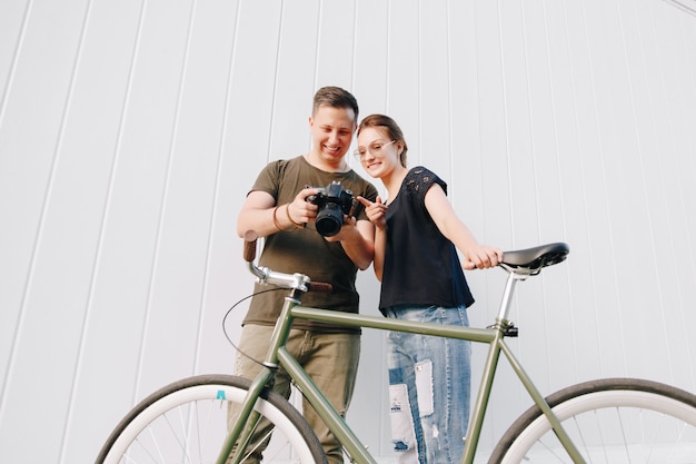 Lächelnder Fotograf und glückliche Frau, die Fotos nach dem Fotoshooting überprüfen und mit Retro-Fahrrad über weißer Wand stehen. Draußen.