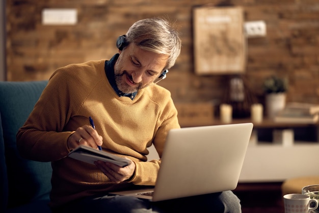 Lächelnder Freiberufler, der sich Notizen macht, während er nachts am Laptop arbeitet