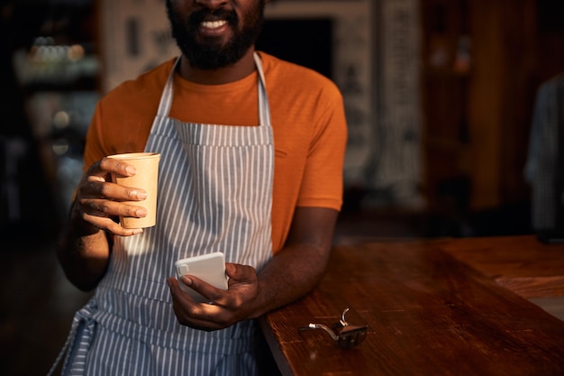 Lächelnder Friseur mit Smartphone und Kaffeetrinken bei der Arbeit