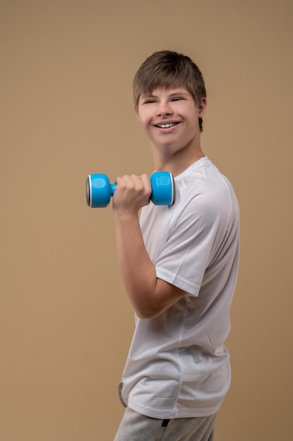 Foto lächelnder, fröhlicher teenager, der die hantel in der hand hält und in die ferne blickt