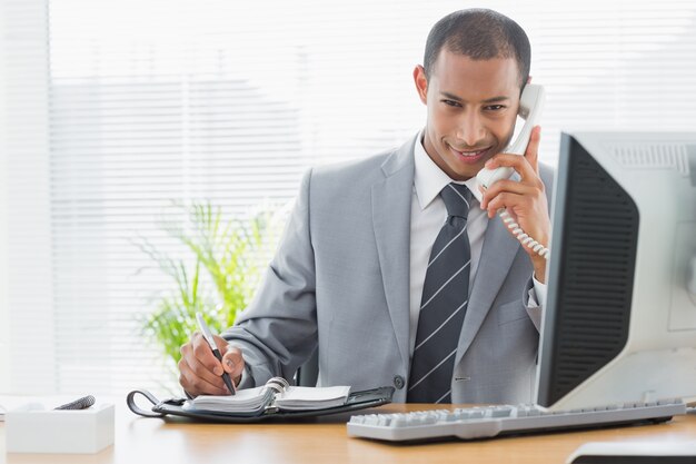 Lächelnder Geschäftsmann, der Computer und Telefon im Büro verwendet