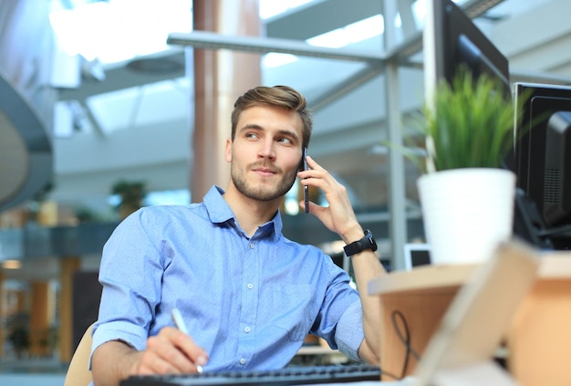 Lächelnder Geschäftsmann, der im Büro steht und Handy benutzt