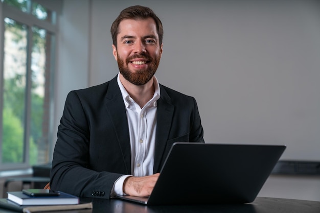 Lächelnder Geschäftsmann in formeller Kleidung, der im Büro am Laptop arbeitet