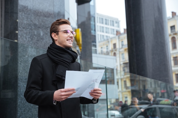 Lächelnder Geschäftsmann mit Dokumenten auf der Straße, der wegschaut
